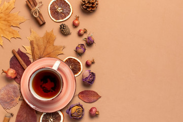 Autumn Flat lay composition. Cup of tea, autumn dry bright leaves, roses flowers, orange circle, cones, decorative pomegranate, cinnamon sticks on brown beige background top view. Autumn, fall concept