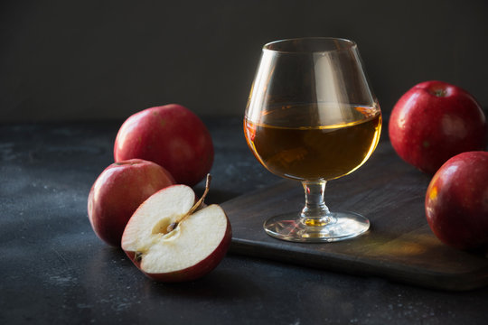 Glass with Calvados brandy and red apples on black. Close up.