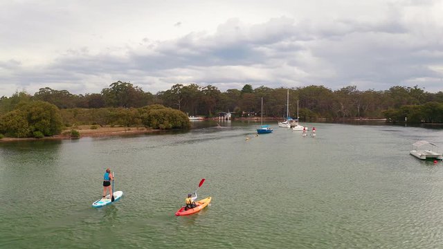 Aerial circling shot of friends kayaking and paddling over Currambene Creek, Australia.