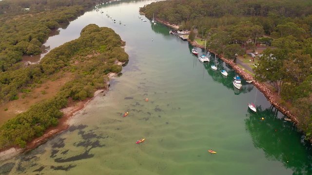 Descending aerial view of kayaks and moored boats in Currambene Creek, Australia.