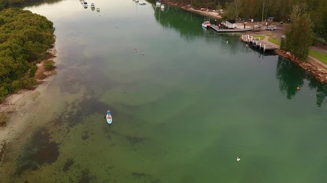 Ascending aerial over person doing paddlesport in Currambene Creek, Australia.