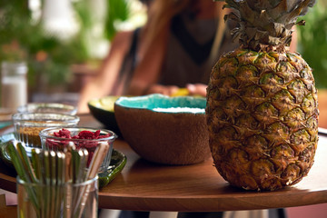 Pineapple stands on a table, along with ingredients for a smoothie bowl