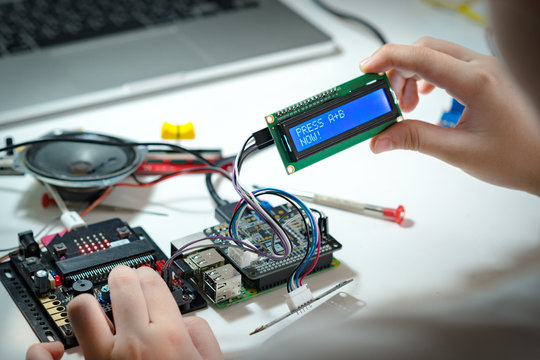 Close up hands of preteen / teenage successfully code and connect blue character LCD display screen to Raspberry pi and Micro:bit in lab. Education, Experiment, Electronics and Science school project