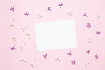 Spring lilac flowers, paper blank on pink background. Flat lay, top view, copy space.