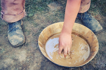 A man washes gold sand in a copper tray. Washing of gold in the tray by American pioneers in...