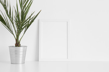 White frame mockup with a palm in a pot on a white table.Portrait orientation.
