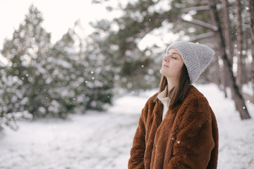 Woman in faux fur coat and woolen hat enjoying snowfall.
