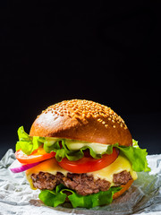 burger with meat, cheese and vegetables on dark black background