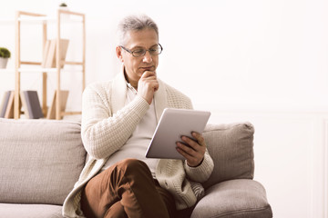 Retired man reading news on tablet at home