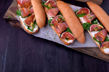 Sandwiches with figs, smoked ham and soft cheese on dark table. Top view
