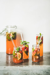 Homemade strawberry and basil lemonade or ice tea in glass tumblers with eco-friendly plastic-free straws on grey concrete table, white wall at background, copy space. Summer refreshing soft drink