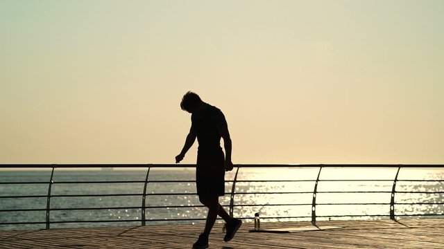 Silhouette of Young strong sportsman doing gymnastic exercise near the sea