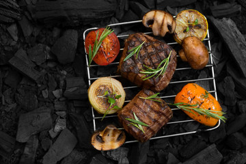 Flat lay of well done meat steak with vegetables on coals