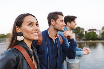 Positive optimistic happy young friends walking outdoors looking at lake.