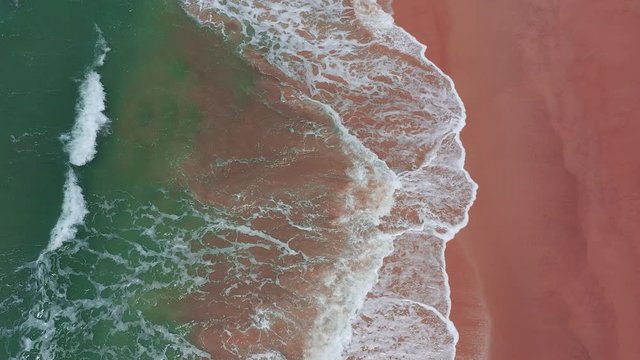 Aerial view of pink beach and blue ocean wave.