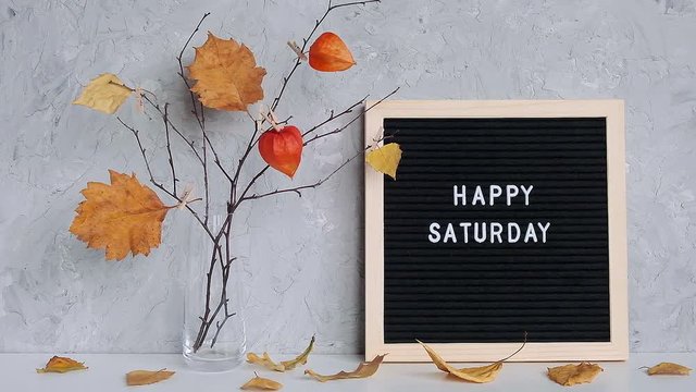 Happy Saturday text on black letter board and bouquet of branches with yellow leaves on clothespins in vase on table Template for postcard, greeting card Concept Hello autumn Saturday.