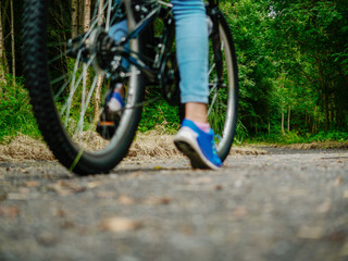 Dark forrest in focus in background. Blurred girl teenager foot and bike on a path leading into the forest. Concept evaluating risk, adventure, scary unknown.