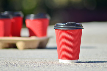 Four red paper coffee cups with black lids on a stand stand on a concrete surface on a black blurred background, one of them stands separately and in front