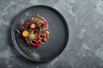 Beef tartare with egg yolk on a gray surface, top view, close-up copy space