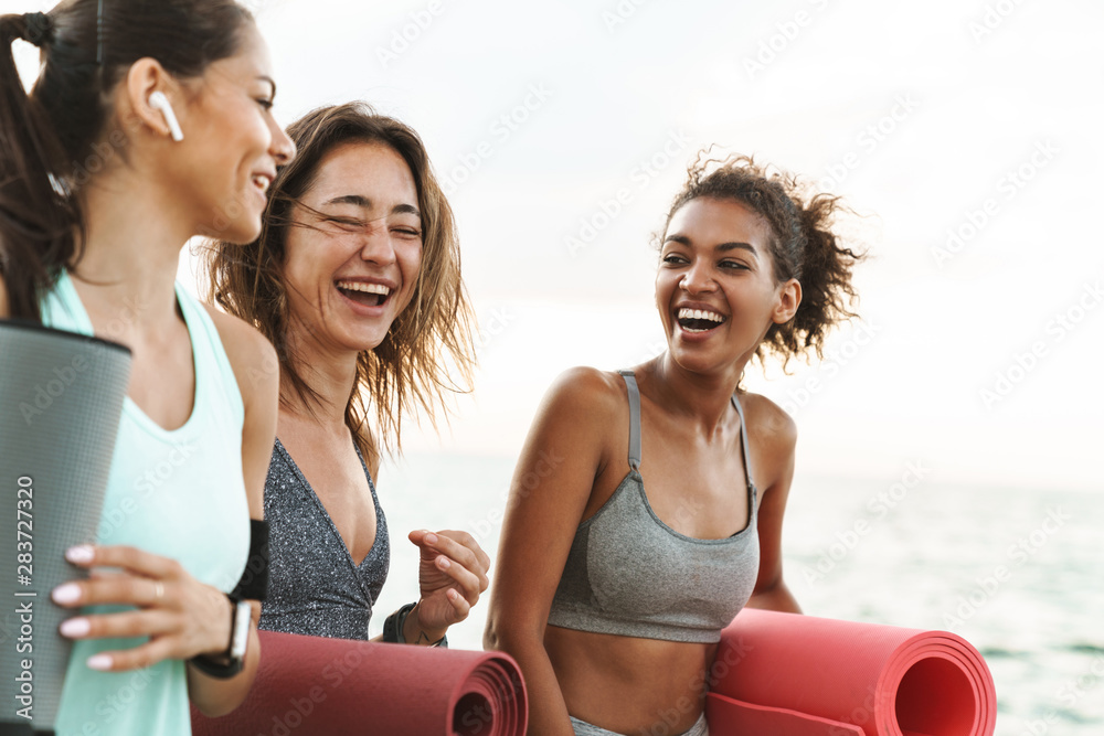 Sticker Three cheerful young sport girls standing at the beach