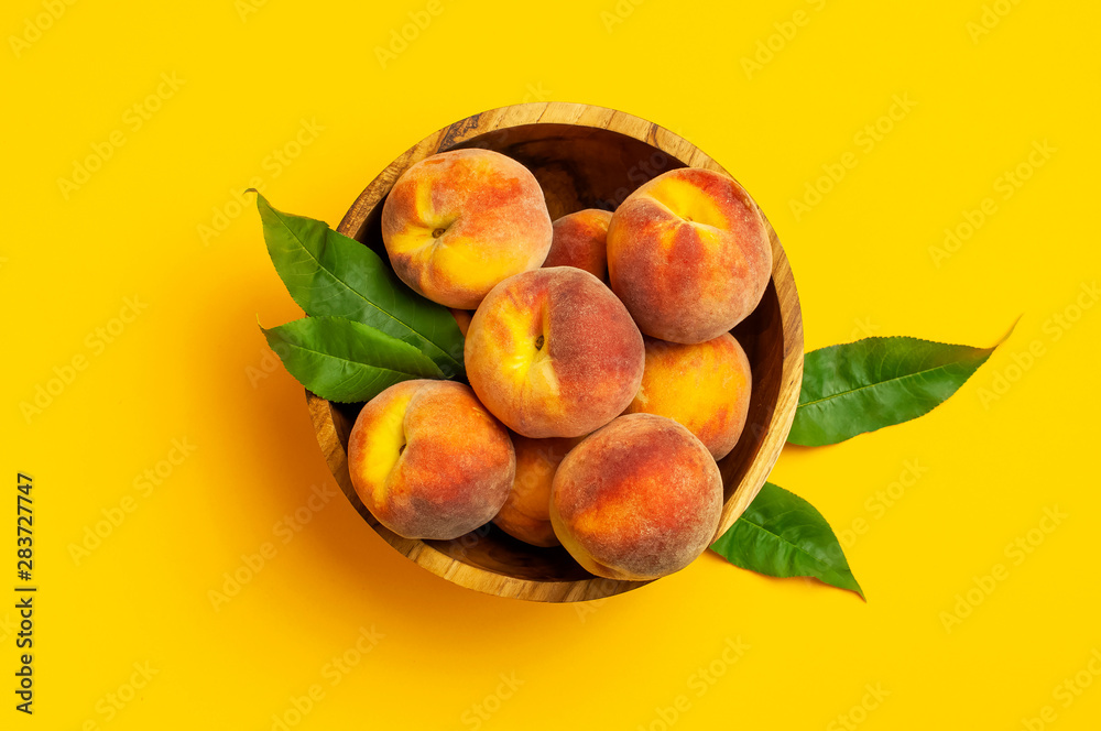 Wall mural flat lay composition with peaches. ripe juicy peaches with green leaves in wooden bowl on yellow bac