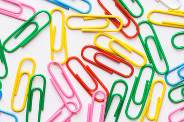 Pattern from multicolored paper clips scattered on white background. School office supplies paperwork documents organization stationery shopping concept.