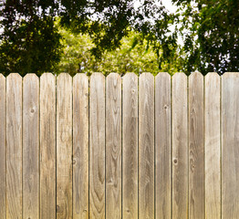 Privacy and security provided by rustic whitewashed wood fence with green shade tree background
