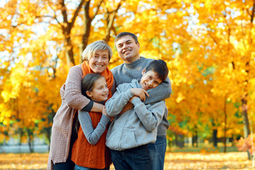 Fototapeta premium Happy family posing, playing and having fun in autumn city park. Children and parents together having a nice day. Bright sunlight and yellow leaves on trees, fall season.