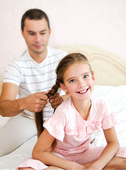 Little girl is smiling while her father is braiding daughter's hair