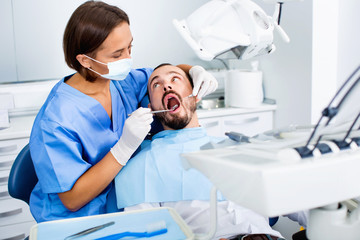 Obraz premium Stomatologist girl in uniform is taking visional inspection of a man