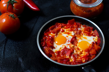 Shakshouka or shakshuka, eggs in a sauce of tomatoes and peppers, top view, dark background, copy space for your text