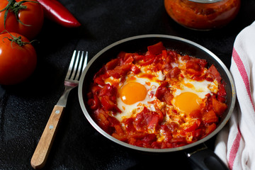 Shakshouka or shakshuka, eggs in a sauce of tomatoes and peppers, top view, dark background, copy space for your text