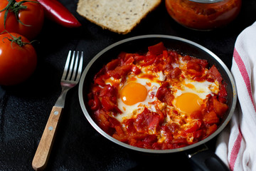 Shakshouka or shakshuka, eggs in a sauce of tomatoes and peppers, top view, dark background, copy space for your text