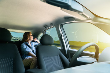 Woman passenger sitting in the backseat and looking out the window when her self-driving car rides on the highway.