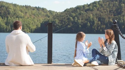 Young family with a little girl spends time fishing at beautiful lake.