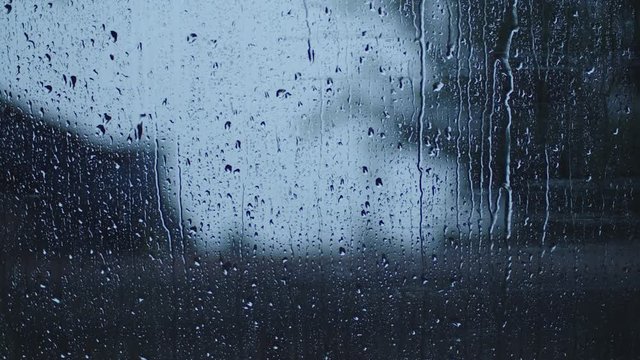 Rain drops on window timelapse hard storm rain autumn weather. Blurred house in the background.