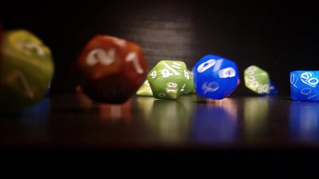 Green, blue & brown polyhedral dice rolling across tabletop at 240fps, against a black background