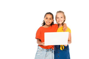 two happy multicultural friends smiling at camera while using laptop together isolated on white