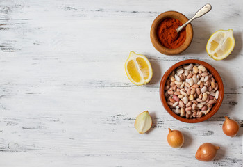 Prebranac ingredients. Balkan baked beans. Serbian, Montenegrin, Bosnian, Croatian, Slovenian cuisine. Uncooked beans, onion, lemon, paprika powder. White wooden background. Top view. Space for text