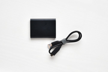 External compact SSD-drive with USB cable for writing, reading and storing data on a white background.