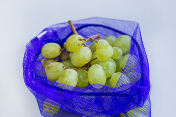 Close up grapes in reusable eco friendly blue bag on light grey table, from market. Zero waste and plastic free concept. Choose plastic free