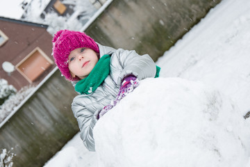 Fototapeta na wymiar Cute little girl is rolling snowball. children make snowman in the yard