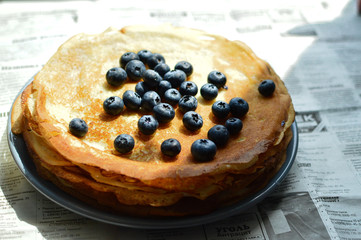 a plate with thin pancakes in bright sunlight with blueberries