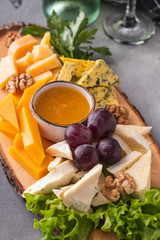 Assorted cheeses  with honey, walnuts and grapes. Tasty cheese plate on a wooden board. Closeup