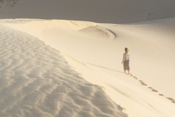 Fototapeta na wymiar Female silhouette walking in desert sand dunes of Mui Ne, Vietnam