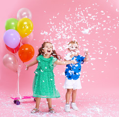 Fototapeta premium Сute little girl and boy joyfully throws confetti isolated on pink background. Celebrating brightful birthday party with colorful balloons. expressing positivity