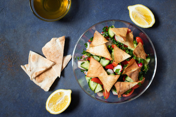 Traditional Fattoush salad  with vegetables and pita bread. Levantine, Arabic, Middle Eastern cuisine. Served in a glass plate with lemon, pita and olive oil. Dark background. Top view. Space for text