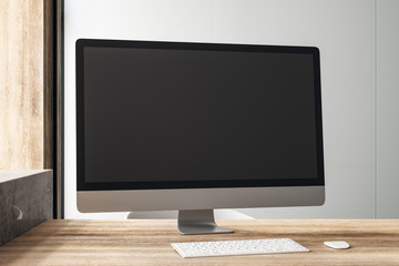 Black blank computer monitor on wooden table in loft style office.
