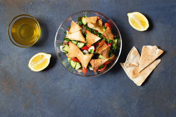 Traditional Fattoush salad  with vegetables and pita bread. Levantine, Arabic, Middle Eastern cuisine. Served in a glass plate with lemon, pita and olive oil. Dark background. Top view. Space for text