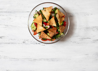 Traditional Fattoush salad  with vegetables and pita bread. Levantine, Arabic, Middle Eastern cuisine. Served in a glass plate with lemon,pita and olive oil. Light background. Top view. Space for text